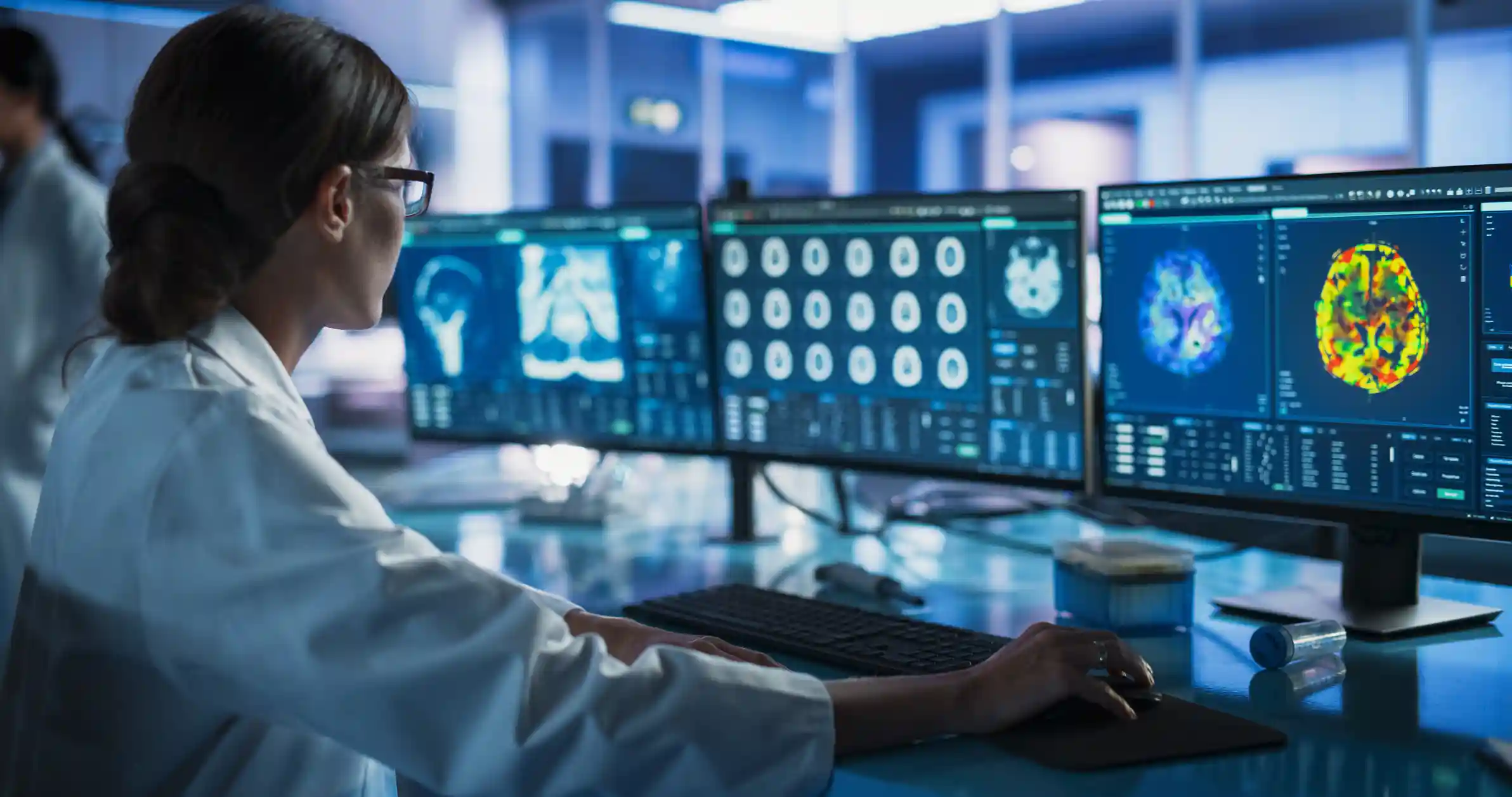 A scientist looking at computer monitors displaying brain scans.